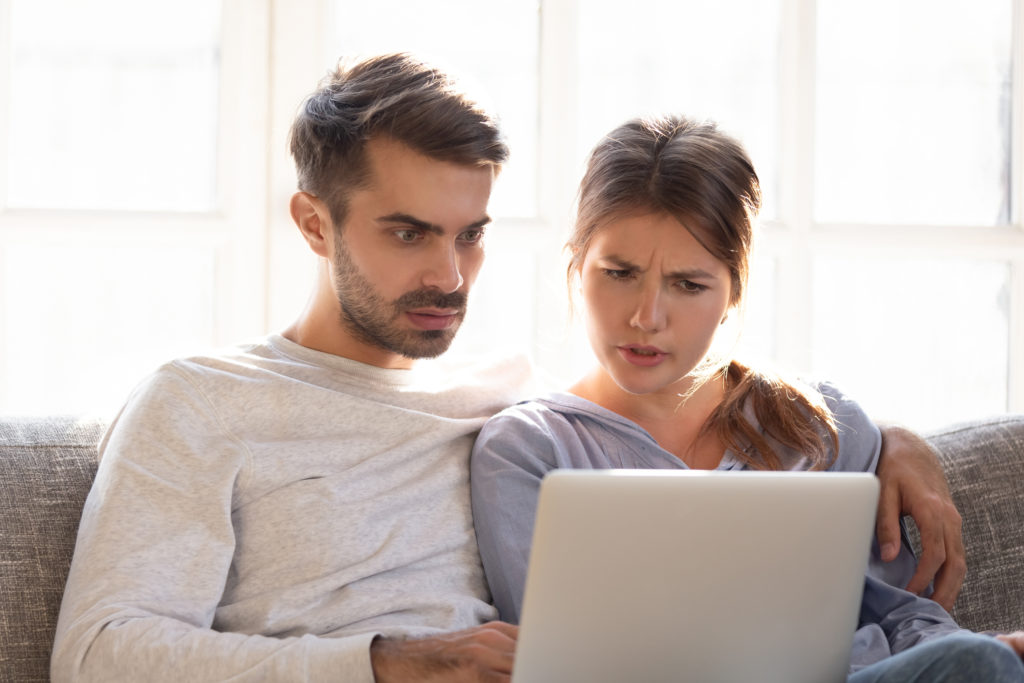 Confused baffled wife and shocked frustrated husband reading online news about stock market